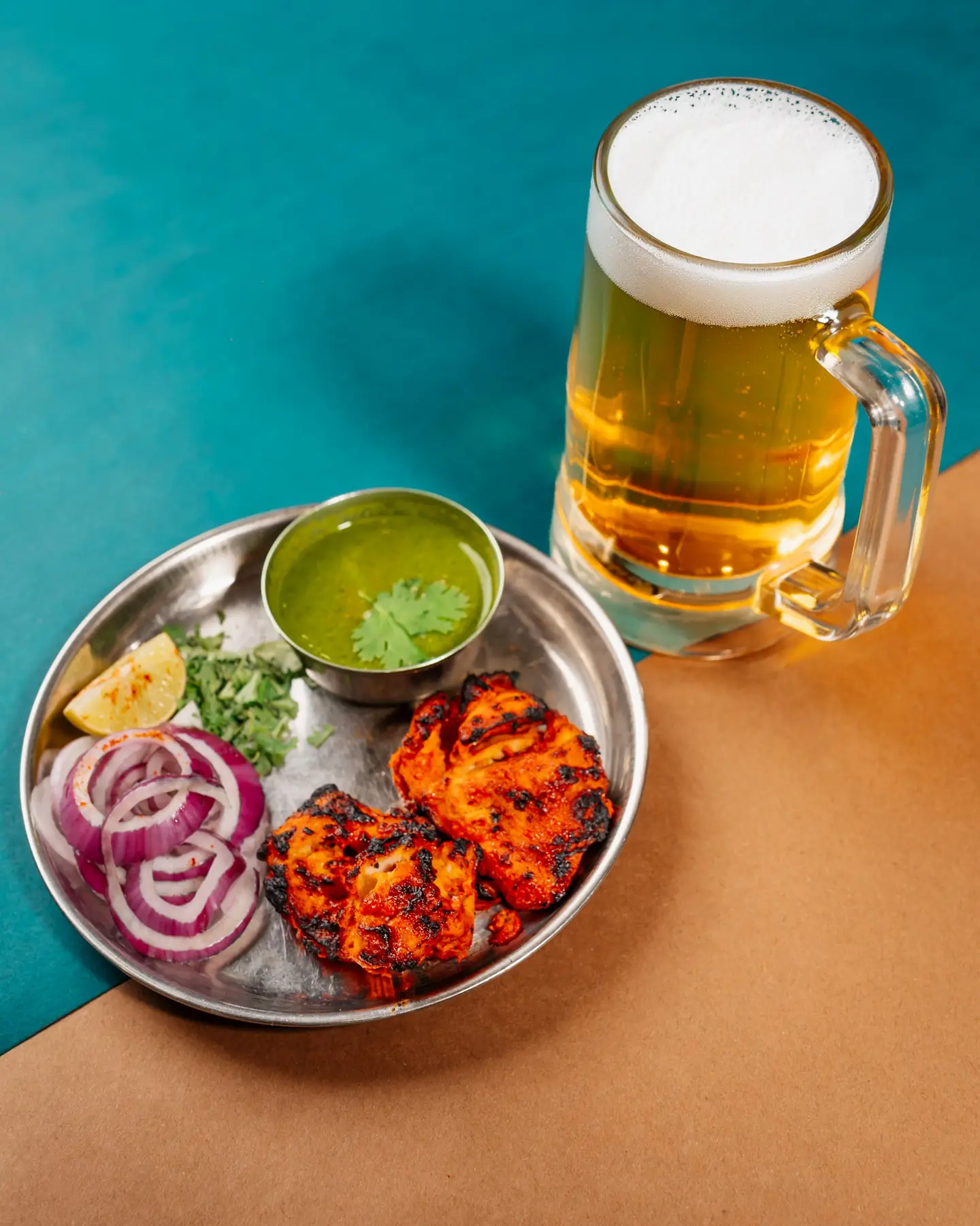 Chicken tikka with onion, lemon and green chutney beside a glass of beer