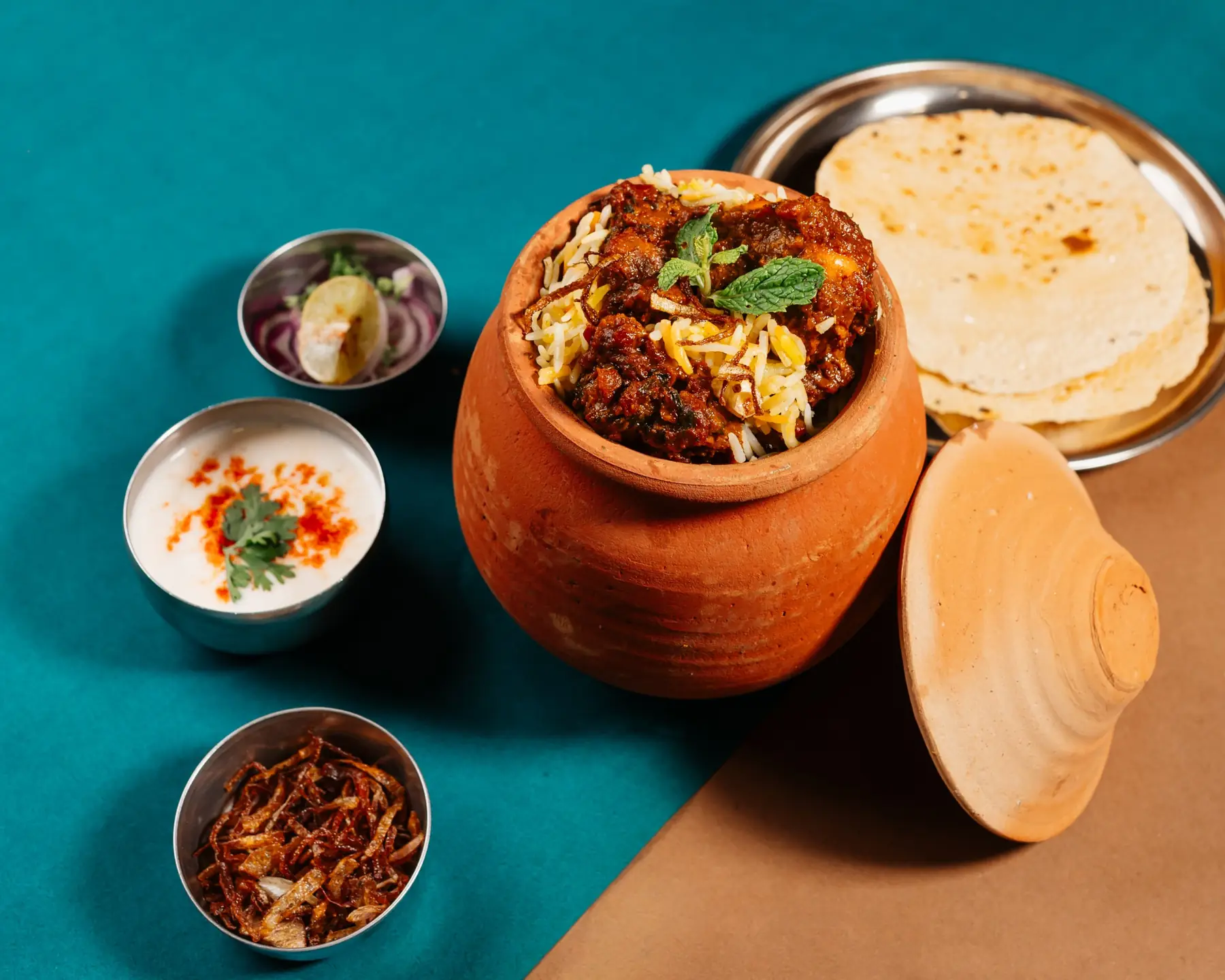 Matka biryani in a clay pot with raita and roti