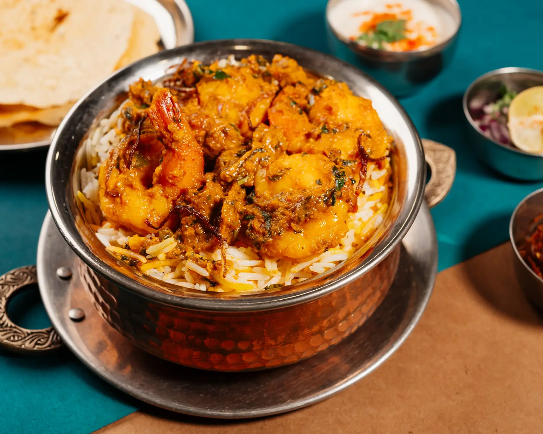 Handi biryani in a copper handi with raita and breads