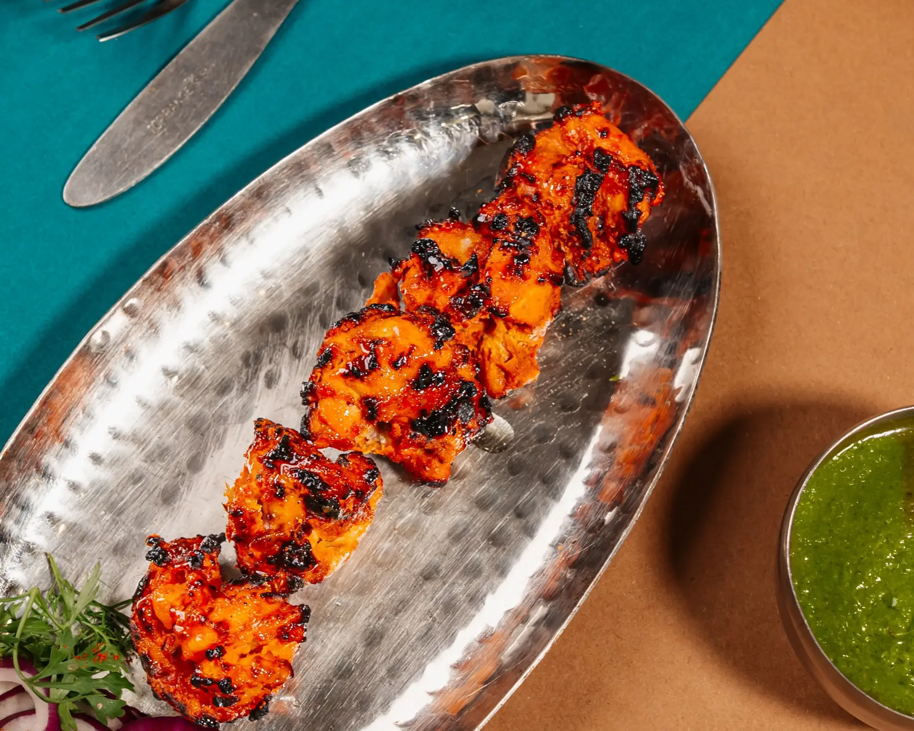 Chicken tikka on a hammered steel platter with green chutney